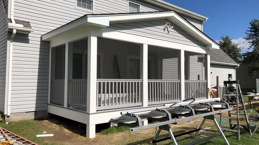 Screened porch with white railing along the back of a home